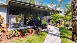 A modern house with a covered patio, surrounded by a garden with various plants and trees. - Poolside Paradise/Suite Serenity: in Naples, FL (Naples)