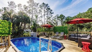 An outdoor swimming pool with a wooden deck, surrounded by lounge chairs and red umbrellas. - Poolside Paradise/Suite Serenity: in Naples, FL (Naples)