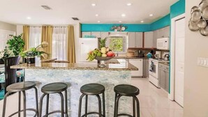 A modern kitchen with a marble island, bar stools, and a fruit bowl. - Poolside/Hibiscus Hideaway:Entire House, Naples FL (Naples)