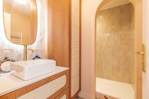Un baño con lavamanos blanco, un espejo y una zona de ducha con paredes de azulejos.