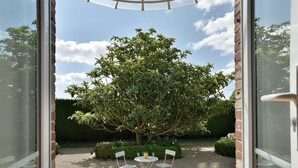 An outdoor seating area with two white chairs and a table, surrounded by a garden with a large tree and hedges. - Les Verts Sapins - Avec grand jardin (Créhen)