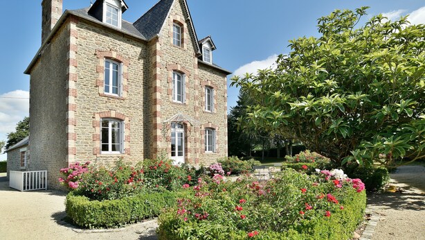 A stone building with a symmetrical facade, multiple windows, and a well-maintained garden with various plants and flowers. - Les Verts Sapins - Avec grand jardin (Créhen)