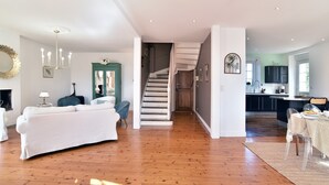A spacious living area with a white sofa, a blue chair, and a staircase leading to a kitchen area. - Les Verts Sapins - Avec grand jardin (Créhen)