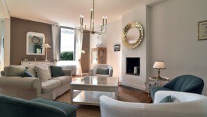 A living room with a glass coffee table, a white sofa, a teal armchair, and a fireplace. - Les Verts Sapins - Avec grand jardin (Créhen)