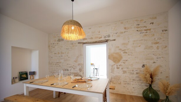 Un coin repas avec une table en bois dressée pour quatre personnes, un luminaire suspendu et des murs en pierre rustique.
