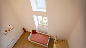Une chambre aménagée en mezzanine avec un lit, une lucarne et une fenêtre.