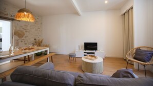 Un salon moderne avec une table à manger en bois, un canapé, une table basse ronde et un téléviseur posé sur un meuble blanc.