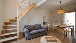 Un espace de vie moderne avec un escalier en bois, un canapé gris, une table à manger avec des bancs et un luminaire suspendu.
