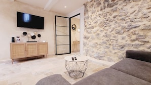 A modern living room with a stone wall, a flat-screen TV, a wooden cabinet, and a round coffee table.