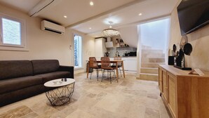A modern living room with a sofa, coffee table, and dining area with chairs. There is a kitchen in the background with a dining table and chairs.