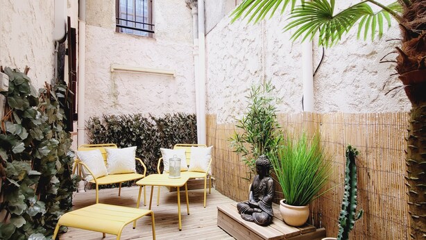 A courtyard with yellow chairs and a statue, surrounded by plants and a bamboo fence.