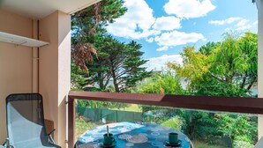 A balcony with a round table, two chairs, and a view of greenery and trees.
