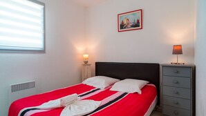 A neatly made bed with a striped red and white bedspread, a small bedside table with a lamp, and a wall-mounted picture.