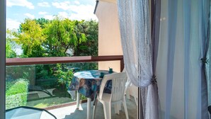 A balcony with a table and chairs, a view of greenery, and a clear sky.