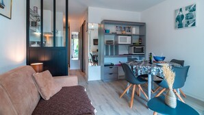 Una sala de estar moderna con un sofá, una mesa de comedor con sillas, una zona de cocina con microondas y una estantería.