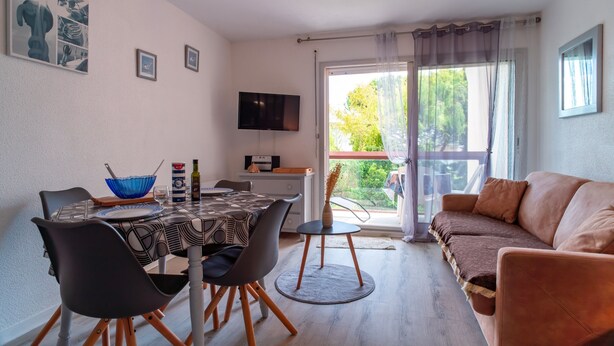 A dining area with a table set for four, a sofa, and a TV mounted on the wall.
