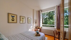 Ein Schlafzimmer mit Bett, Schreibtisch und einem Fenster mit Blick auf Bäume.