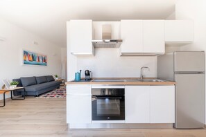 Une cuisine compacte dotée d’un four encastré, d’un réfrigérateur en acier inoxydable et d’un plan de travail en bois.