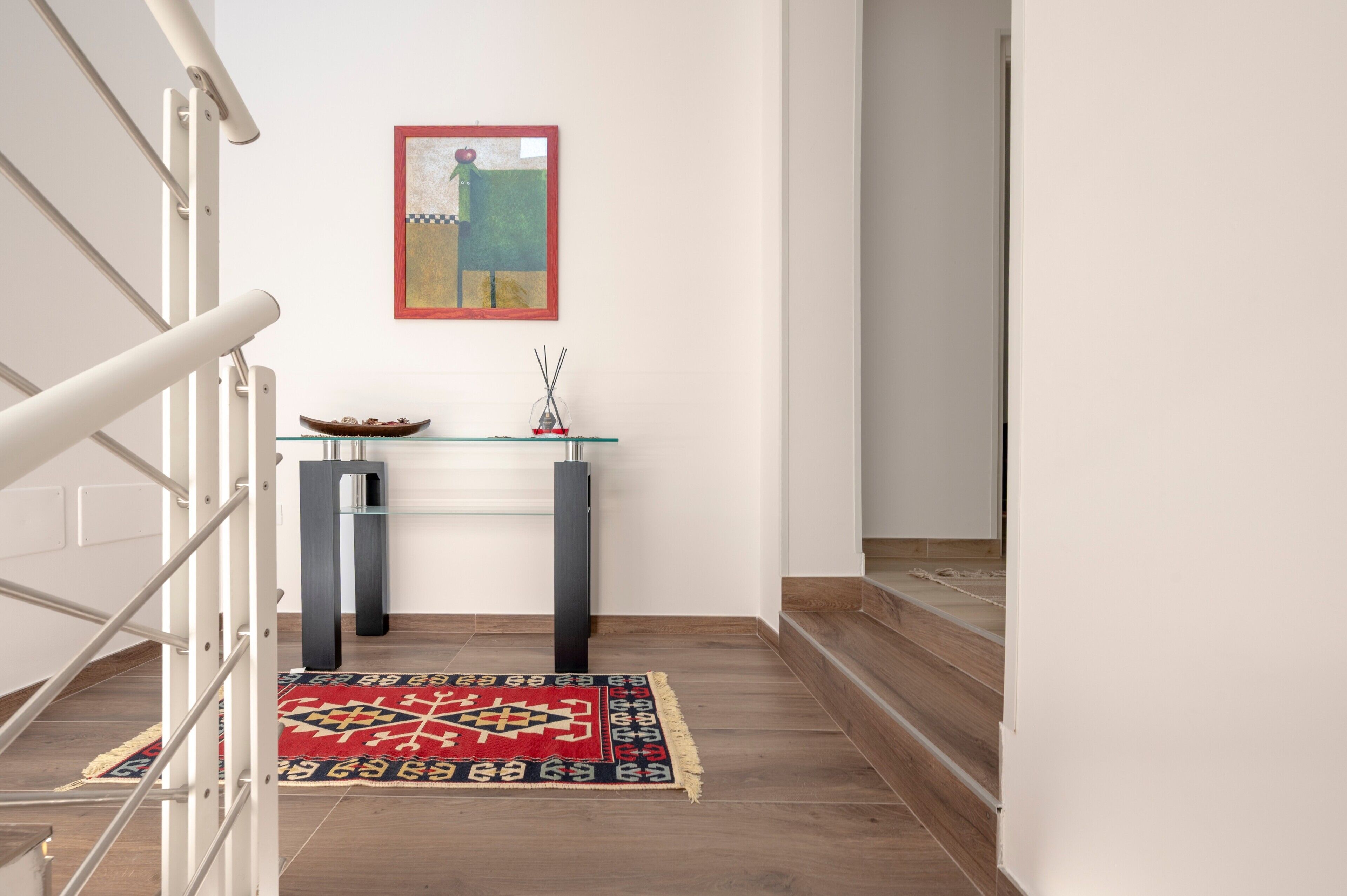 A staircase leading to a landing with a glass-top console table, a framed artwork, and a patterned rug.