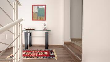 A staircase leading to a landing with a glass-top console table, a framed artwork, and a patterned rug.