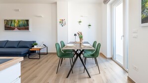 A modern living room with a sofa, a dining table with chairs, a painting on the wall, and a window with a view. - Apartment 'Ingrosso Suites - Green' with Private Terrace, Wi-Fi and Air Conditioning (Castri di Lecce)