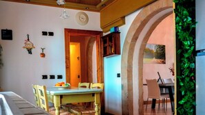 Un comedor con una mesa y sillas de madera, una cocina con refrigerador, y vistas al exterior a través de un arco.