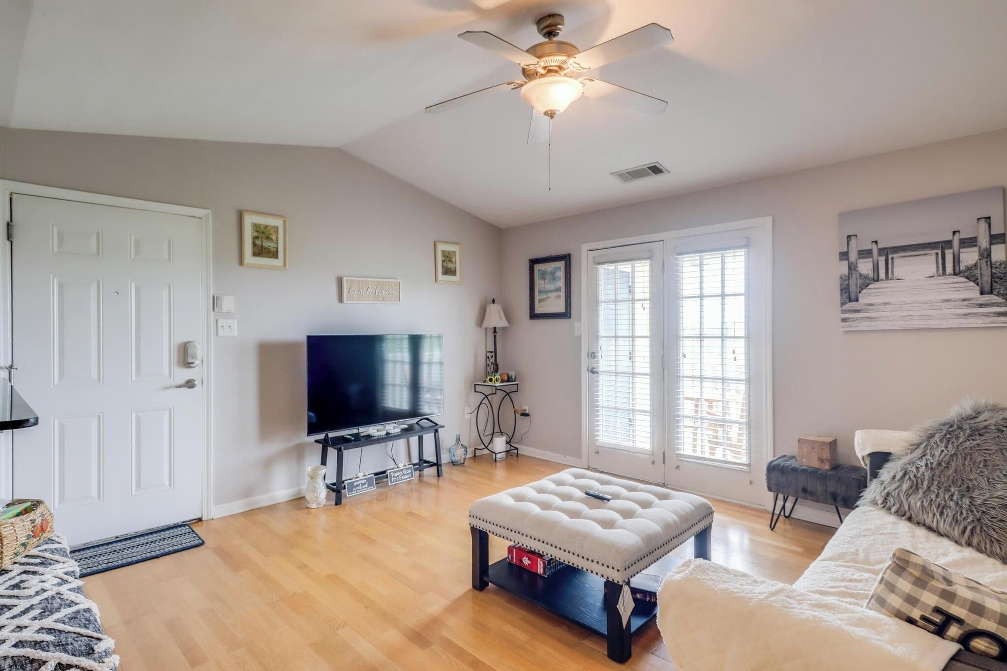 A living room with a television, a ceiling fan, a sofa, and a large window.