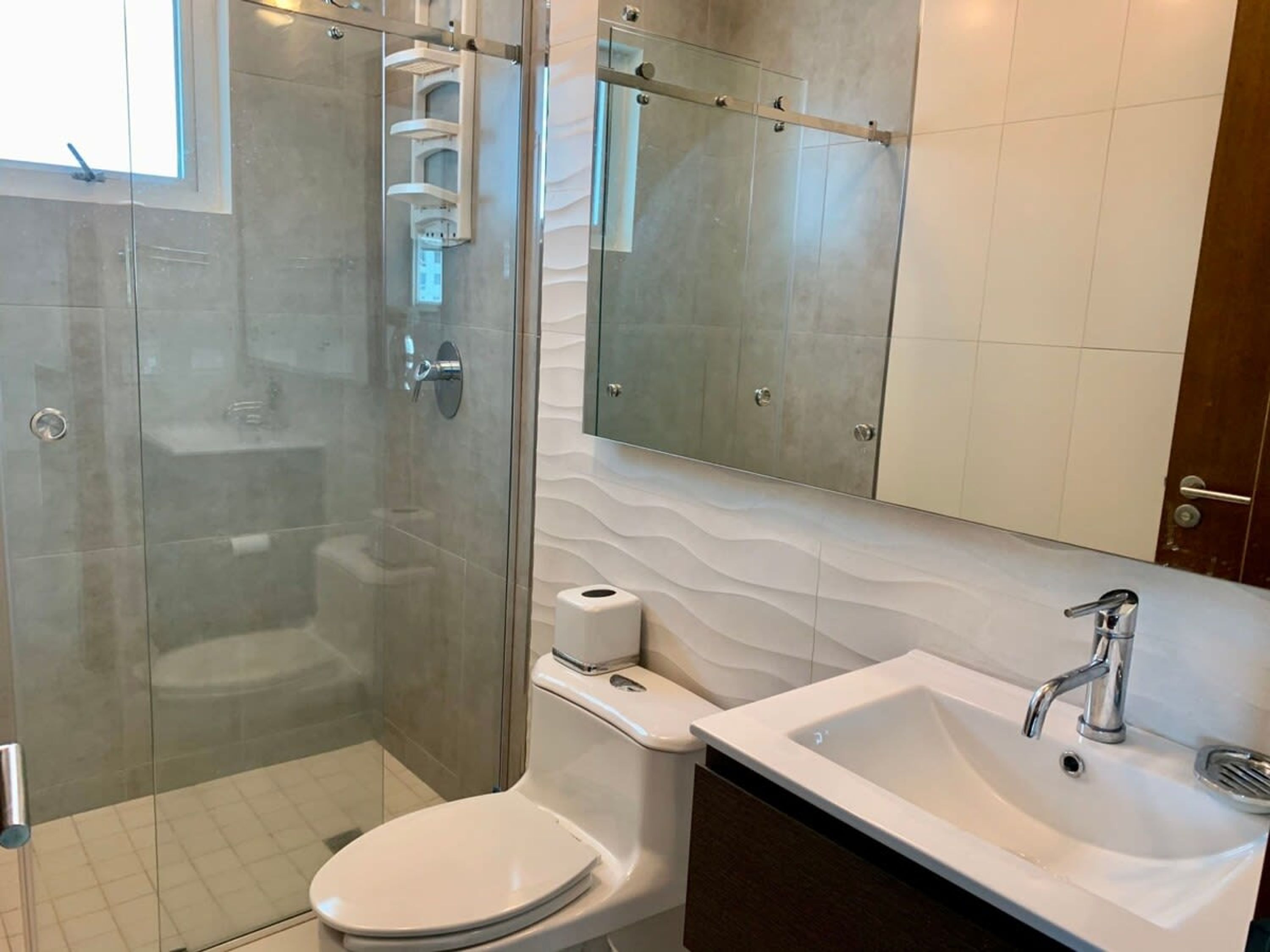 A modern bathroom with a glass-enclosed shower, a toilet, a sink, and a mirror.