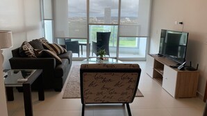 A modern living room with a sofa, a coffee table, a TV, and a balcony with a view of the city. - Garden Cafe I Spacious 1 Bed Apt With Park View (Panama City)