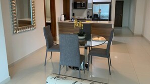 A modern dining area with a glass table, grey chairs, and a decorative mirror. - Garden Cafe I Spacious 1 Bed Apt With Park View (Panama City)