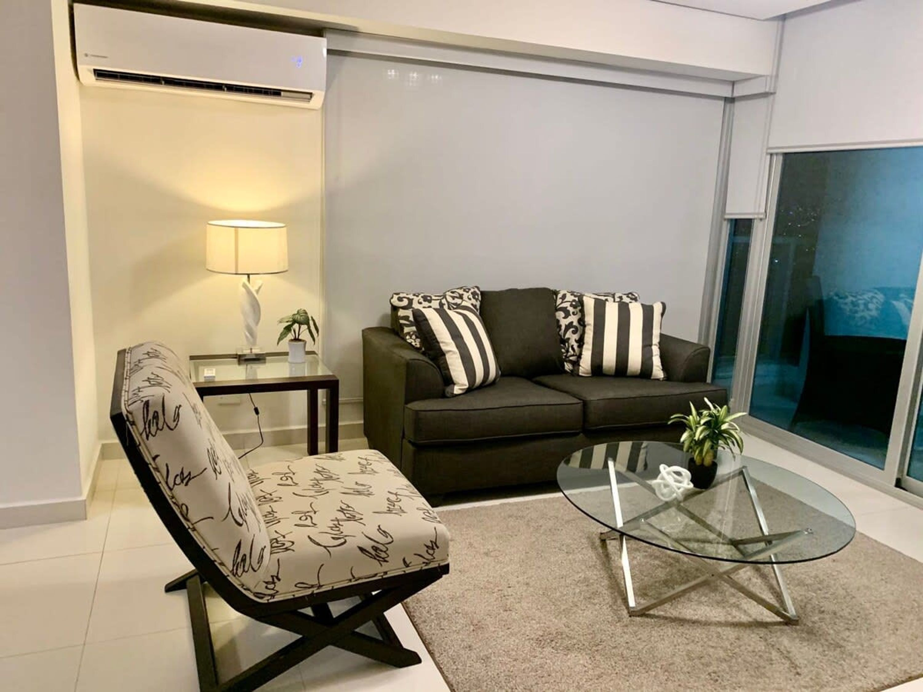 A modern living room with a sofa, a chair, a glass coffee table, and a lamp.