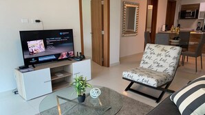 A living room with a TV, a glass coffee table, a sofa, and a chair. - Garden Cafe I Spacious 1 Bed Apt With Park View (Panama City)