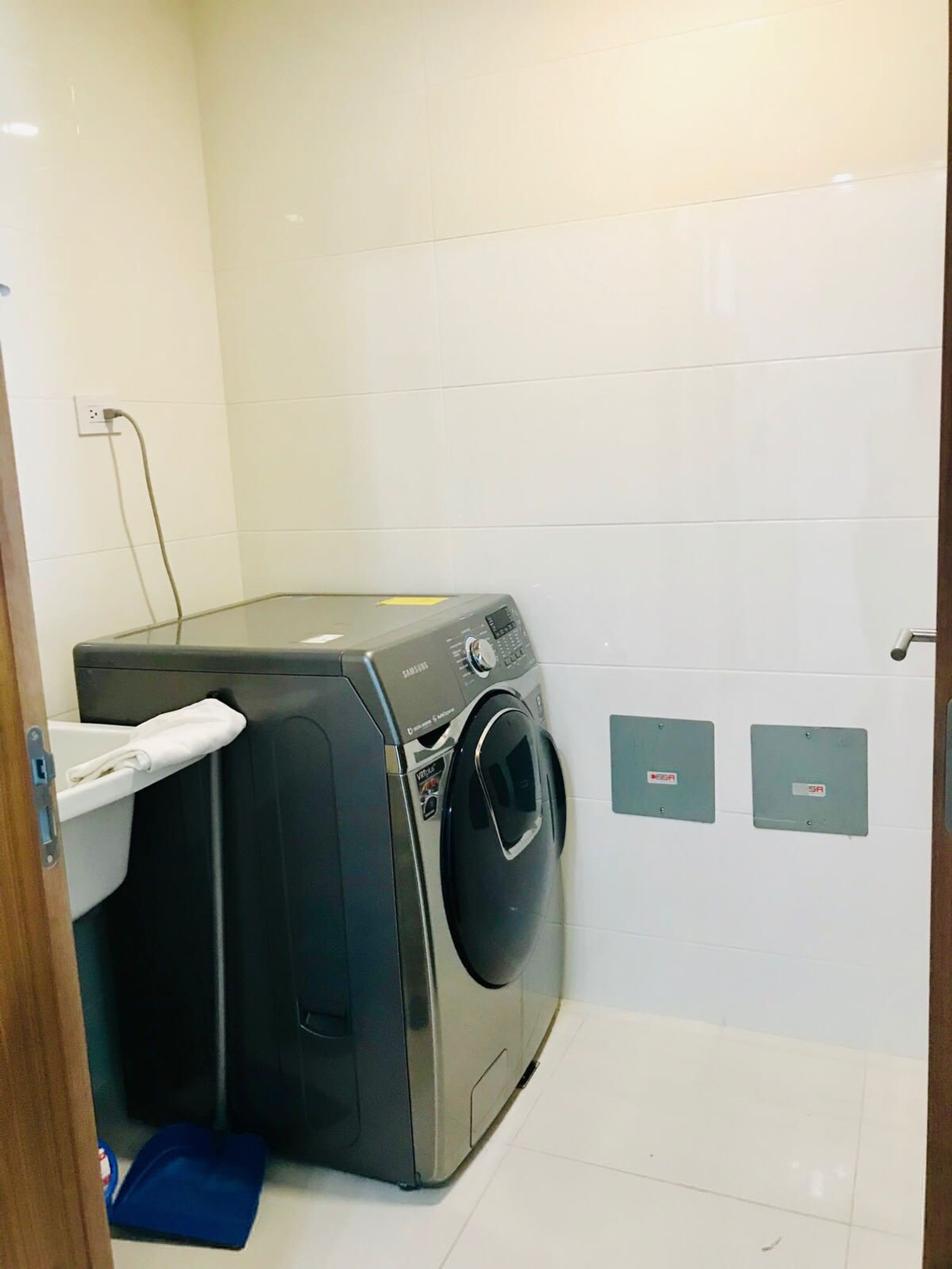 A compact laundry room with a washing machine, a small sink, and two electrical outlets on the wall.