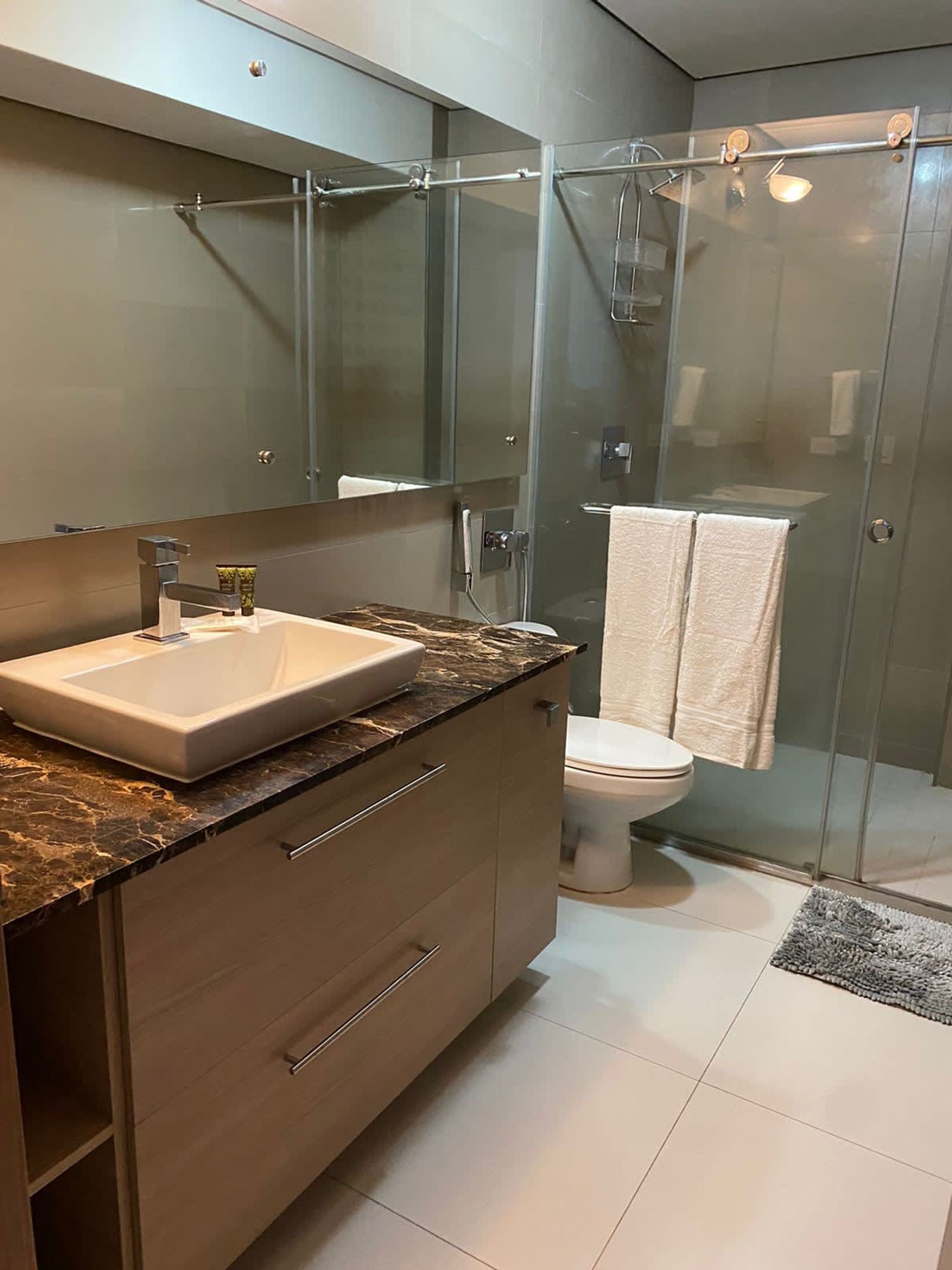 A modern bathroom with a glass shower enclosure, a marble countertop, and a white toilet.
