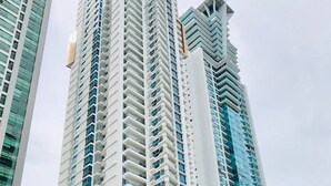 Un immeuble moderne de grande hauteur, doté d’une façade en verre remarquable, entouré de palmiers et comprenant un espace de stationnement.