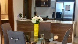 Une cuisine moderne dotée d’appareils électroménagers en acier inoxydable, une table à manger en verre avec des chaises, et un vase jaune orné de fleurs.