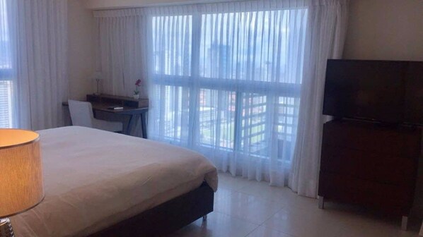Habitación de hotel con cama, escritorio, silla, televisor y ventana con cortinas.