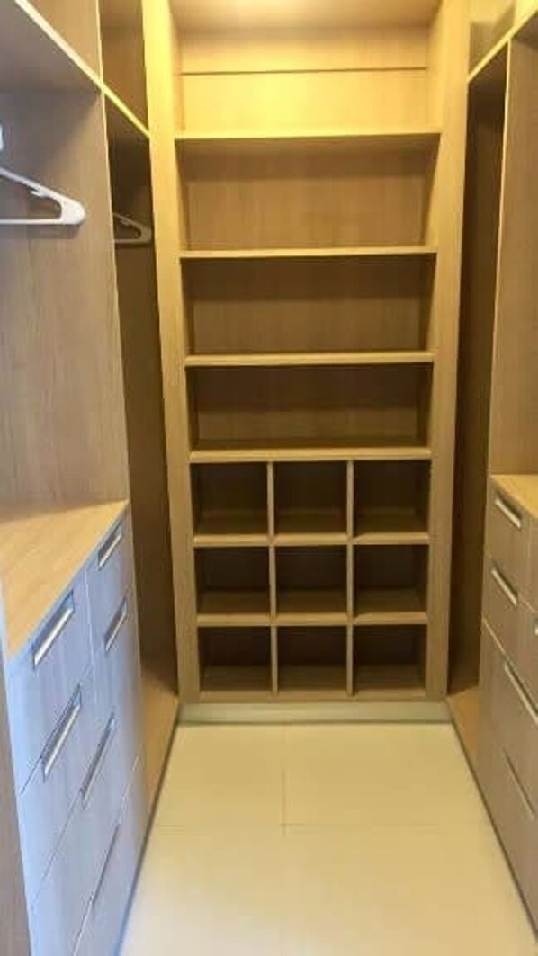A walk-in closet with multiple shelves and drawers, featuring a light wood finish and a neutral color palette.