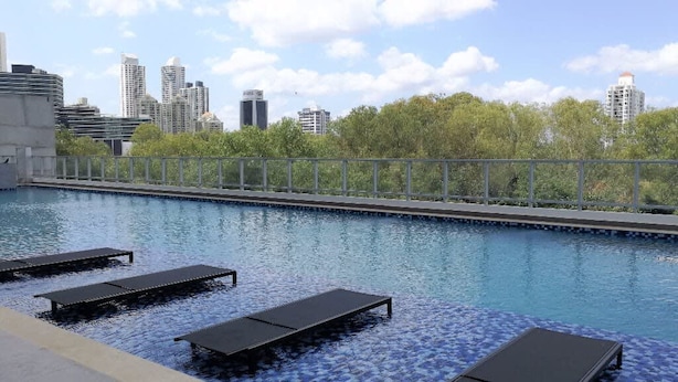 Une piscine sur le toit, avec des chaises longues, et une vue sur les toits de la ville en arrière-plan.