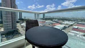 Un balcón con mesa y silla, con vistas a un paisaje urbano con rascacielos y cielo despejado.