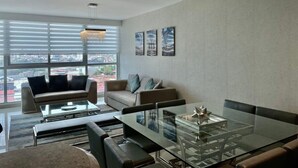 Una sala moderna con una mesa de comedor de vidrio, dos sofás y vistas a la ciudad a través de amplias ventanas.