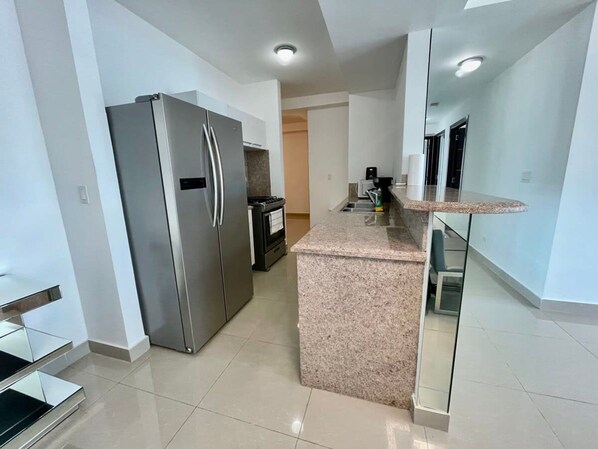 A modern kitchen with a stainless steel refrigerator, granite countertop, and a built-in oven.