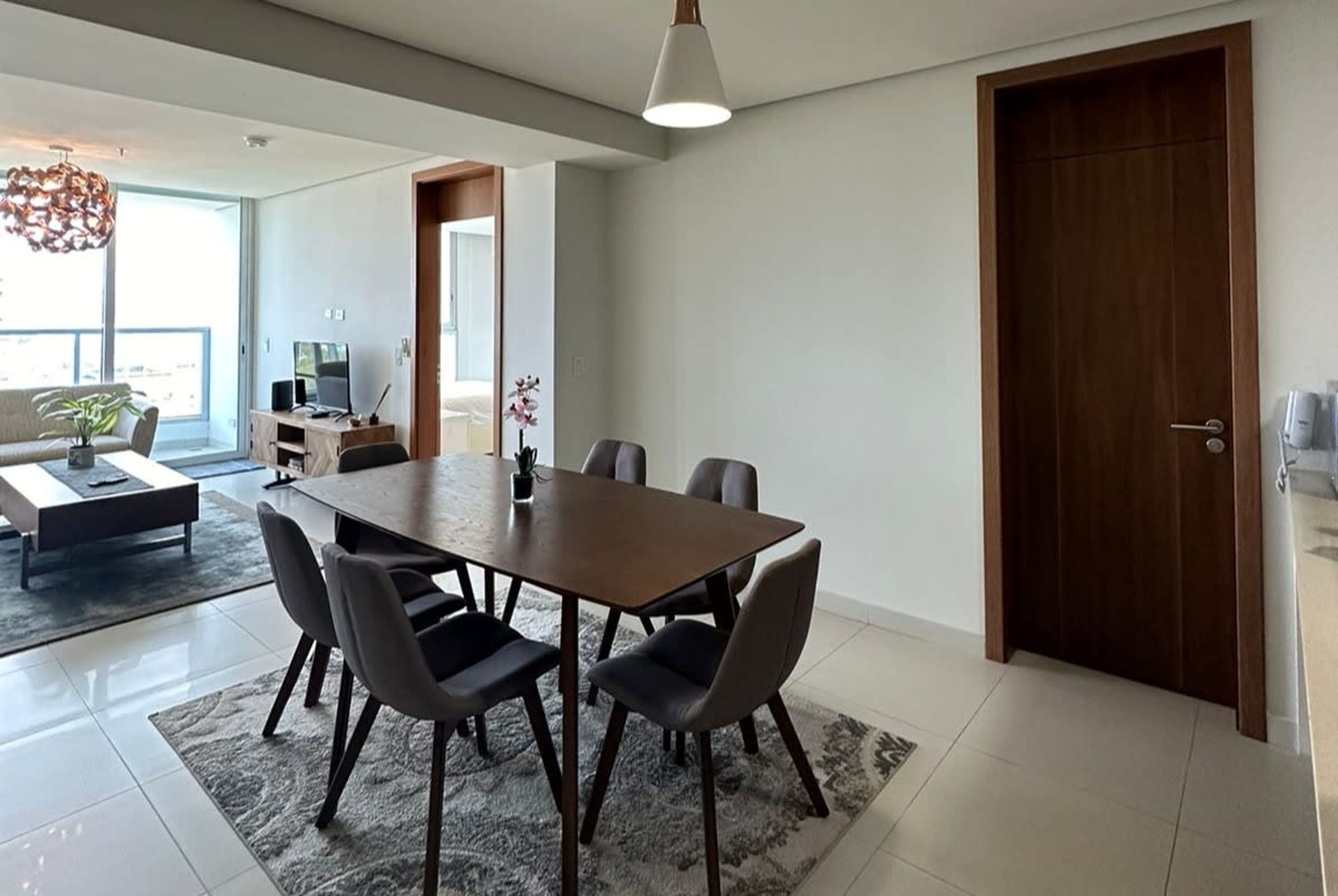 Uma zona de refeições moderna com uma mesa retangular e seis cadeiras, uma máquina de café e uma televisão ao fundo.