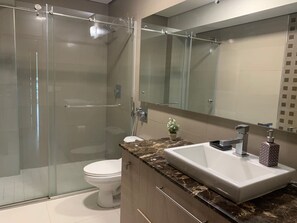 A modern bathroom with a glass-enclosed shower, a white toilet, a marble countertop, a sink with a faucet, and a mirror above the sink. - Miramar I Comfortable 1bdr With Park View (Panama City)