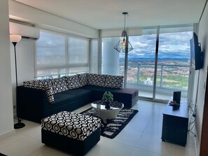 A modern living room with a black and white patterned sofa, a coffee table with a plant, and a large window offering a city view. - Miramar I Comfortable 1bdr With Park View (Panama City)