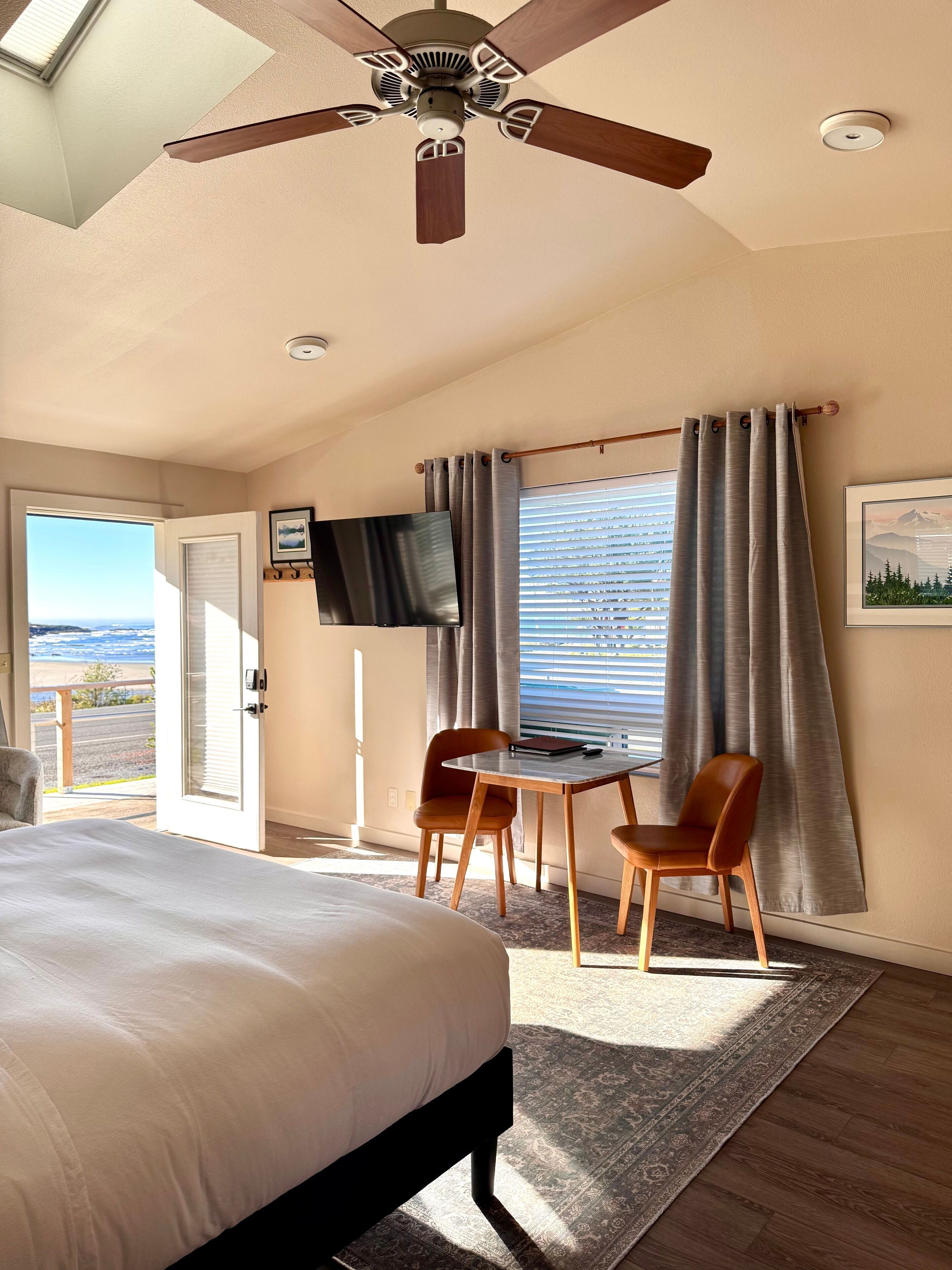 Une chambre d’hôtel avec un lit, un bureau, deux chaises, une télévision et une fenêtre avec des rideaux.