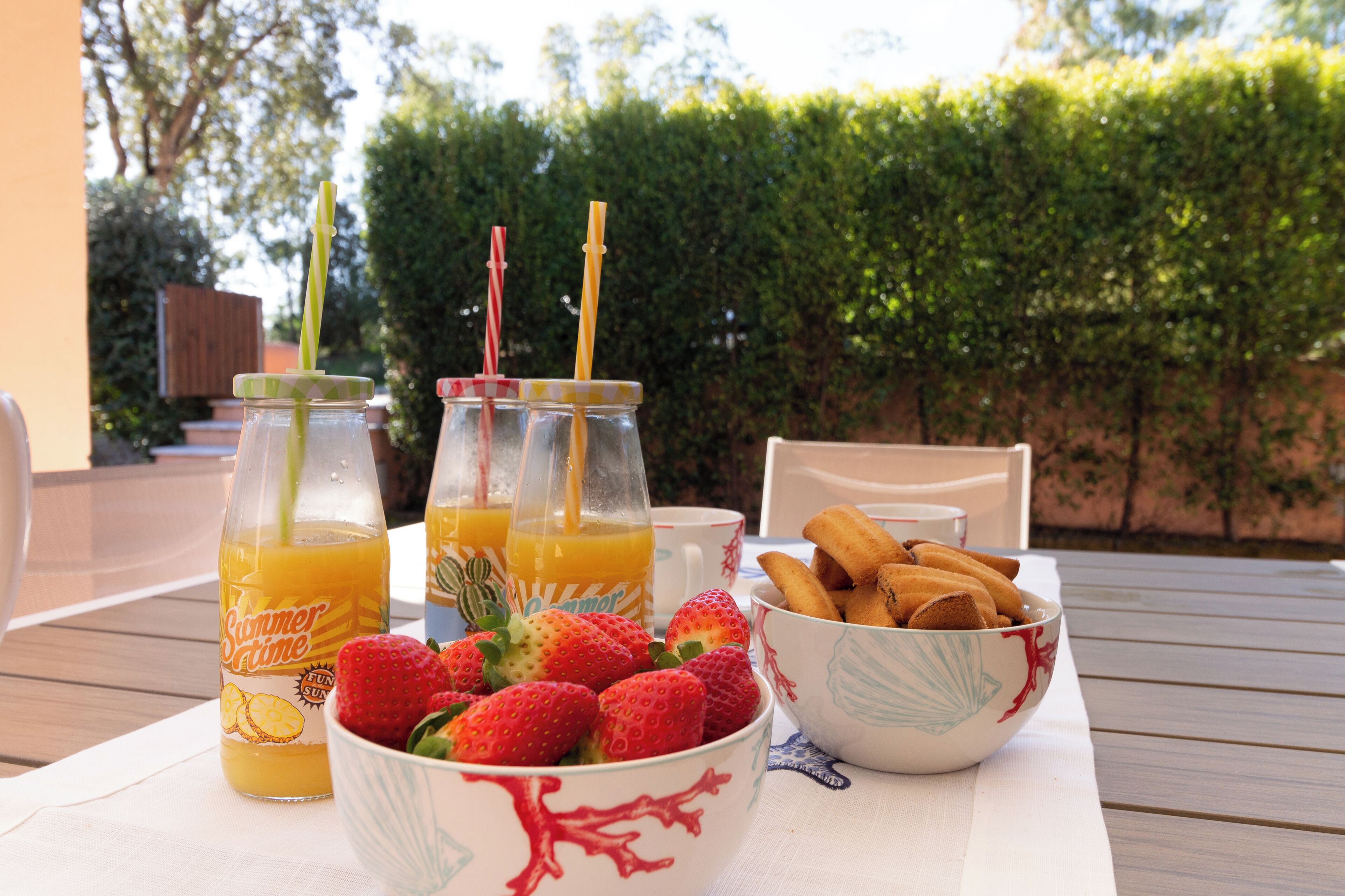 Una mesa con alimentos para el desayuno, incluyendo fresas, un bol de pasteles y dos botellas de zumo de naranja.