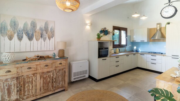 A modern kitchen with white cabinets, a central island, a hanging light fixture, and a wall clock. - Relax with the whole family in this quiet and elegant accommodation (Santa Margherita di Pula)