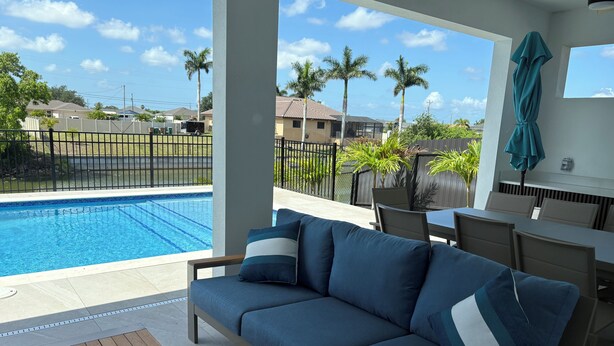 A poolside area with a blue sofa, wooden table, and a dining table with chairs. - Gorgeous, new 3-bedroom, 3 bathroom house. heated Pool in Cape Coral , sleeps 8 (Cape Coral)