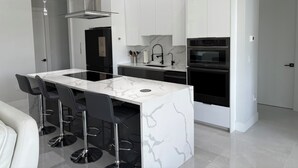 A modern kitchen with white cabinets, a black refrigerator, a built-in oven, and a marble countertop. - Gorgeous, new 3-bedroom, 3 bathroom house. heated Pool in Cape Coral , sleeps 8 (Cape Coral)
